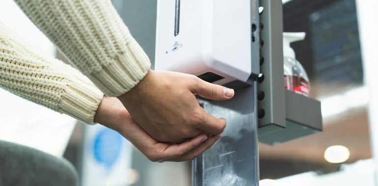 Osoba dezynfekuje ręce, korzystając z automatycznego dozownika na płyn do dezynfekcji PERS